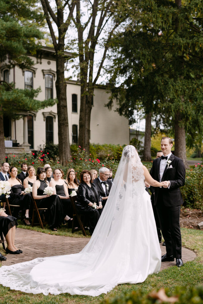 Bride and groom holding hands during garden ceremony at Peterson Dumesnil House Louisville wedding
